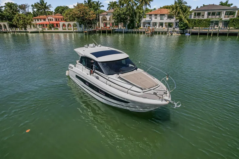 Slide: The Image of 2020 Jeanneau NC 37 yacht cruising on a serene waterfront with luxury homes in the background. - 9