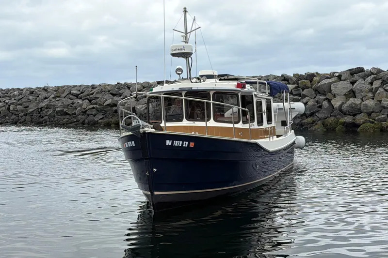 Slide: The Image of 2014 Ranger Tugs R-25 SC boat docked near rocky shoreline under cloudy sky. - 1