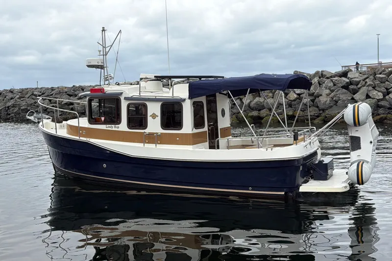 Slide: The Image of 2014 Ranger Tugs R-25 SC boat docked near rocky shoreline under cloudy sky. - 4