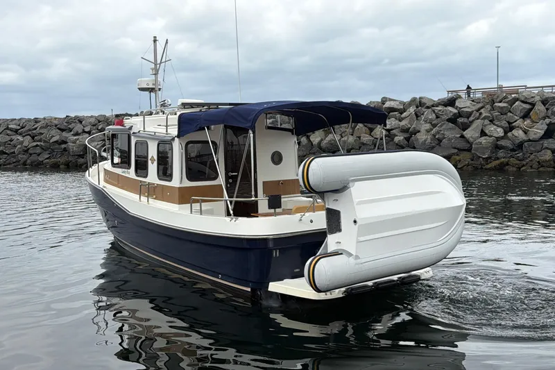 Slide: The Image of 2014 Ranger Tugs R-25 SC boat with inflatable dinghy, docked near rocky shoreline. - 6