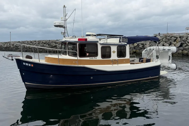 Slide: The Image of 2014 Ranger Tugs R-25 SC boat docked in calm waters, with rocky shoreline background. - 7