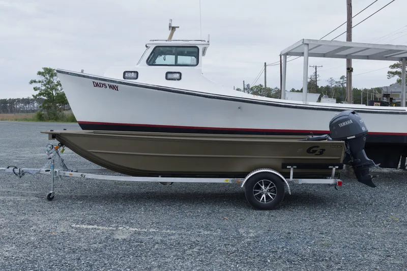 The Image of 2026 G3 Gator Tough 18 DK boat on trailer, parked beside a larger boat. - 1