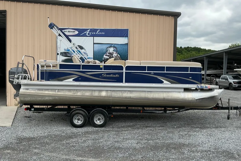 The Image of 2012 Godfrey Sweetwater 2486 C pontoon boat on trailer, parked outside a building. - 1