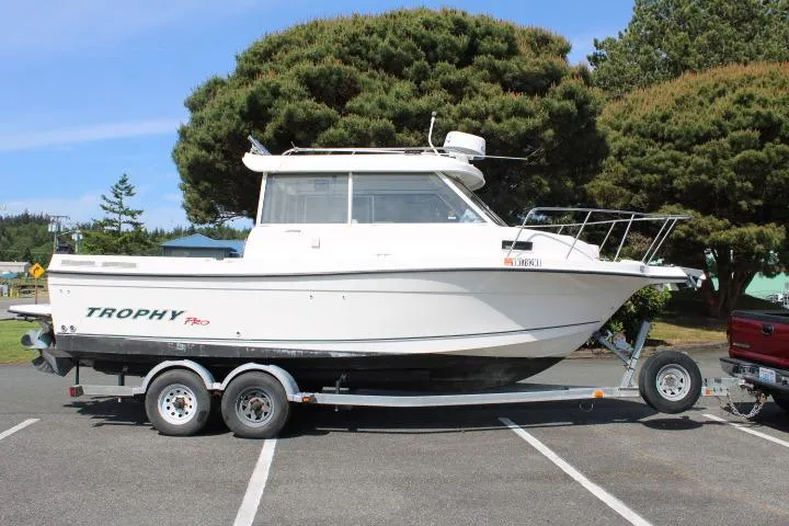 The Image of 2006 Trophy 2359 Pro boat on trailer in parking lot, surrounded by trees. - 0