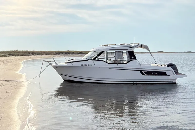 The Image of 2022 Jeanneau NC 795 boat anchored on a sandy beach, calm waters. - 0