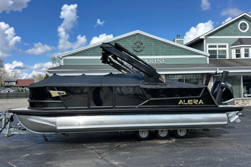 Slide: The Image of 2026 Alera M23L pontoon boat with black cover, parked outside a marine building. - 48