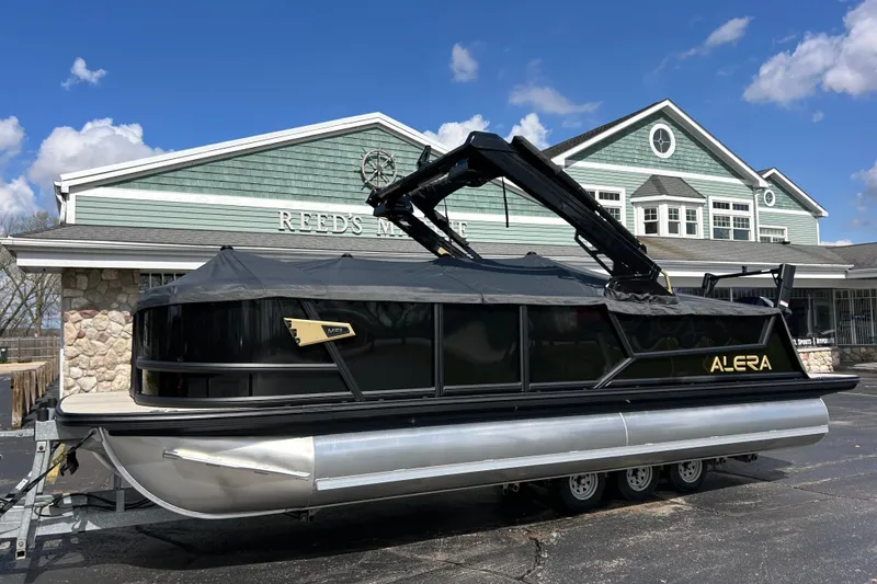 Slide: The Image of Alera M23L 2026 pontoon boat parked outside Reed's Marine under a clear blue sky. - 49