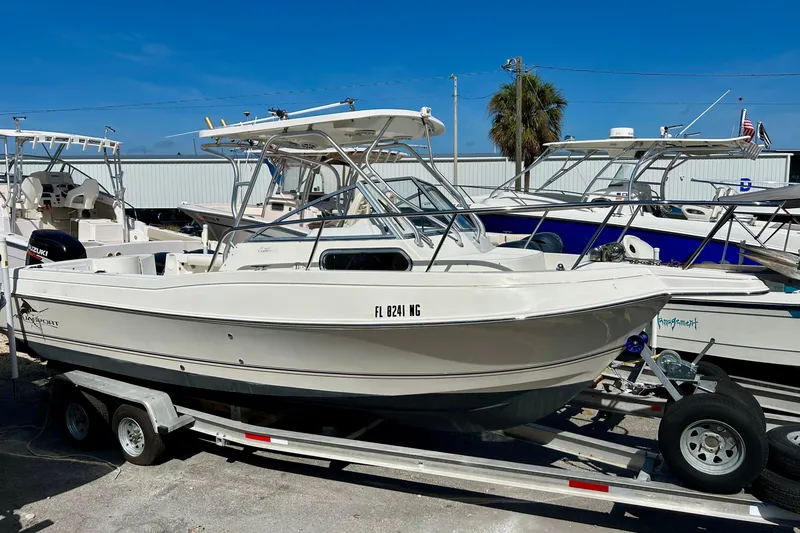 The Image of 2005 Aquasport 250 Explorer boat on trailer, parked in marina under clear blue sky. - 1