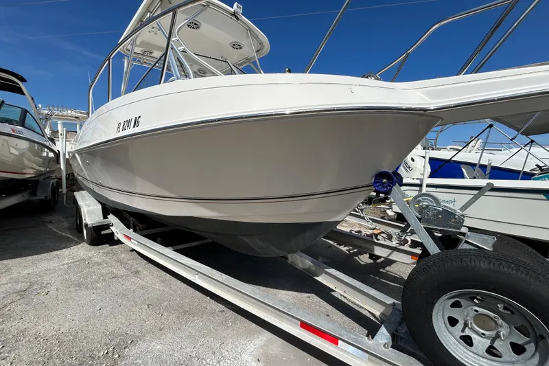 Slide: The Image of 2005 Aquasport 250 Explorer boat on trailer, parked outdoors under clear blue sky. - 16