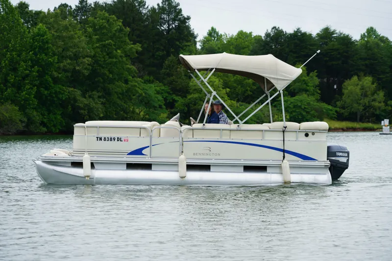 Slide: The Image of 2005 Bennington II 207L pontoon boat cruising on a lake with lush green trees. - 2