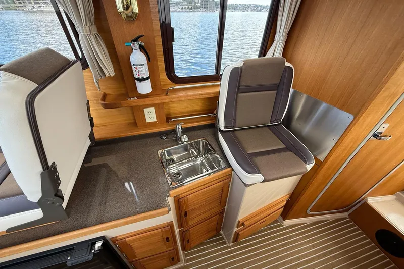 Slide: The Image of 2014 Ranger Tugs R-27 interior with sink, seating, and wooden cabinetry. - 52
