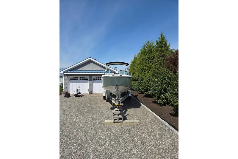Slide: The Image of 2018 Boston Whaler 230 Vantage boat on trailer in driveway, near garage and greenery. - 33