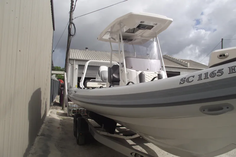 Slide: The Image of 2024 Highfield Sport 760 boat on trailer, parked beside a building under cloudy skies. - 2