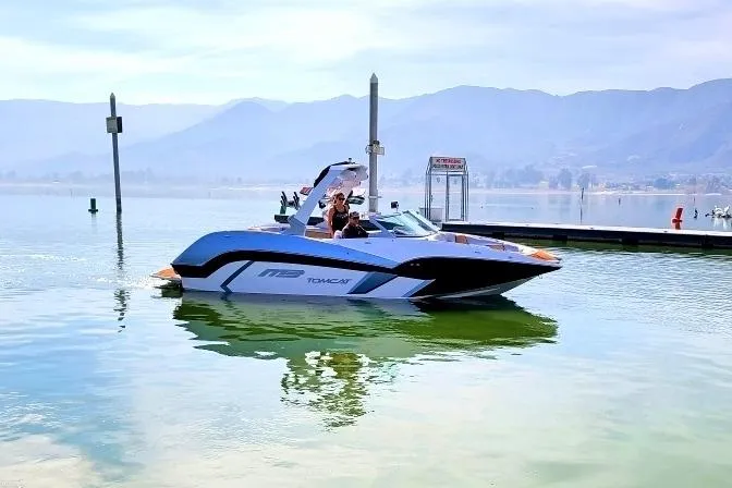 Slide: The Image of 2021 MB F24 Tomcat boat on a serene lake with mountains in the background. - 2
