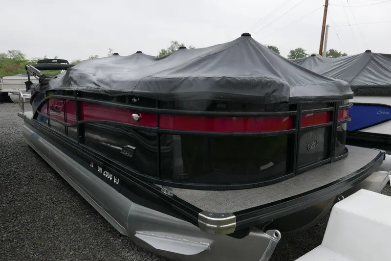 Slide: The Image of 2022 Barletta CORSA 23QC pontoon boat with protective cover, parked on gravel. - 12