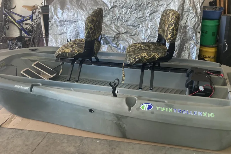 The Image of 2023 Freedom Twin Troller X10 boat with dual camouflage seats in a garage setting. - 1