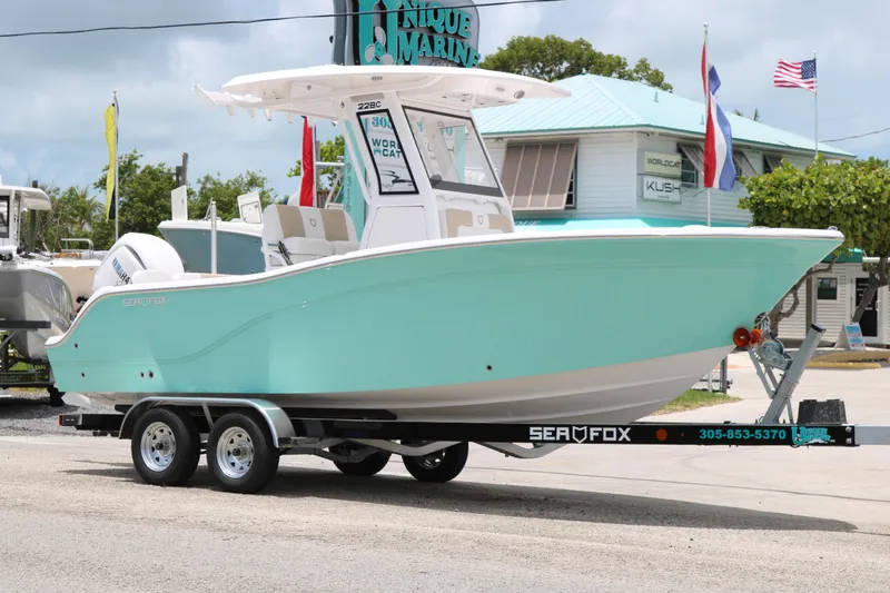 Slide: The Image of 2026 Sea Fox 228 Commander boat on trailer, displayed outdoors near marina flags. - 2