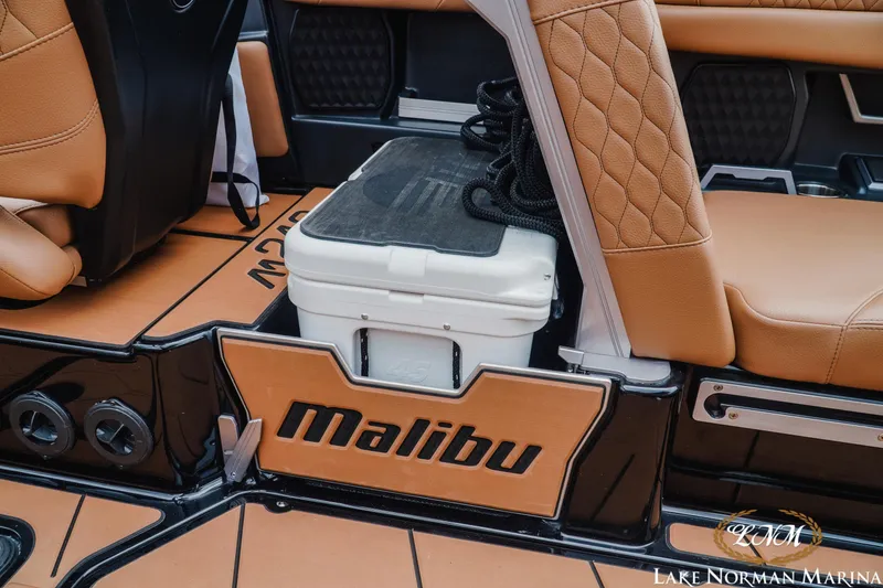 Slide: The Image of 2021 Malibu M240 boat interior with tan leather seats and cooler storage. - 15