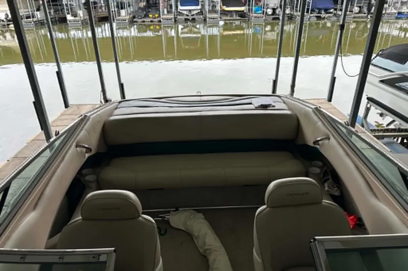 Slide: The Image of 1997 Crownline 225 BR boat interior at dock, featuring beige seating and calm waters. - 7