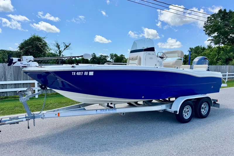 The Image of 2017 NauticStar 211 Coastal boat on trailer, blue hull, parked on a sunny day. - 1