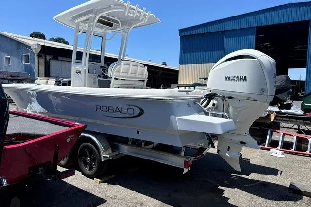 The Image of 2023 Robalo 246 Cayman boat with Yamaha engine, parked on a trailer near a warehouse. - 0