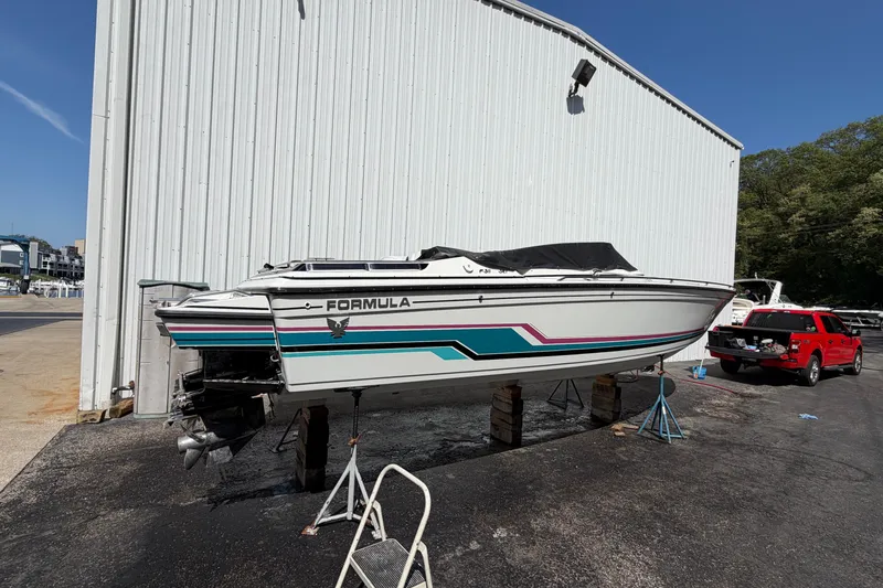 Slide: The Image of 1991 Formula 311 SR-1 boat on stands, white with colorful stripes, near a large building. - 10