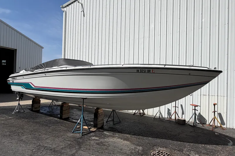 Slide: The Image of 1991 Formula 311 SR-1 boat on stands, white hull with colorful stripes, parked outside a warehouse. - 13