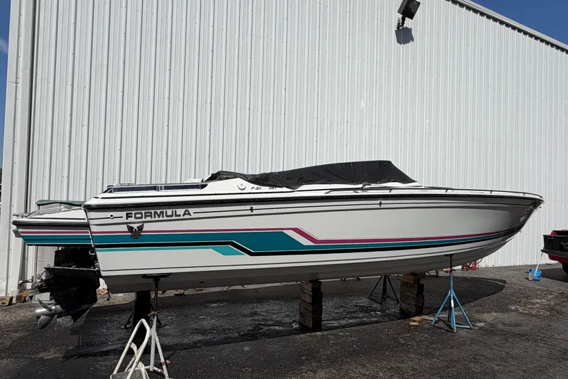 Slide: The Image of 1991 Formula 311 SR-1 boat on stands, white with teal and pink accents, near a metal building. - 14