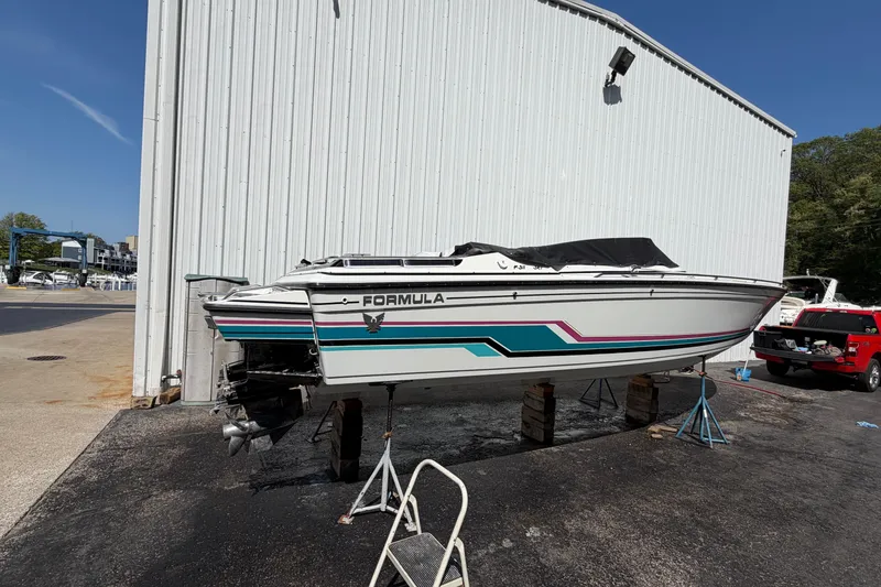 Slide: The Image of 1991 Formula 311 SR-1 boat on stands, white with teal and pink stripes, near a warehouse. - 9