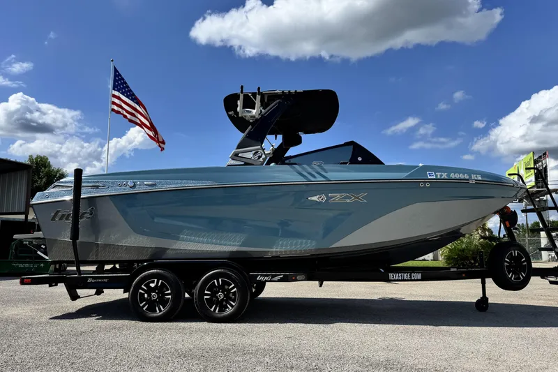 Slide: The Image of 2021 Tigé 23ZX boat on trailer, American flag in background, under a partly cloudy sky. - 3