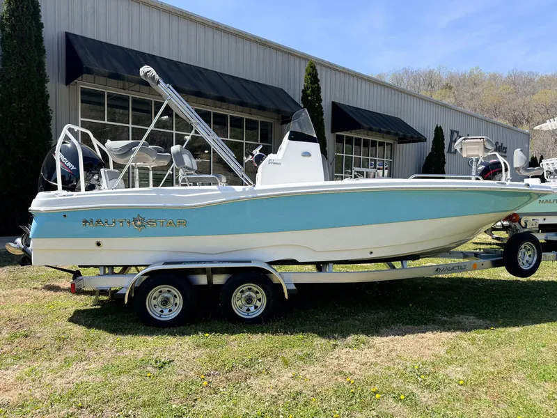 The Image of 2024 NauticStar 211 Hybrid boat on trailer in front of building. - 1