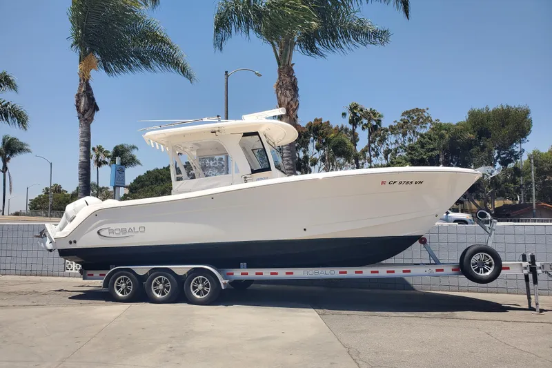 The Image of 2017 Robalo R302 Center Console boat on trailer, parked near palm trees. - 0