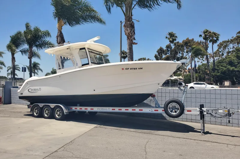 Slide: The Image of 2017 Robalo R302 Center Console boat on trailer, parked near palm trees. - 1