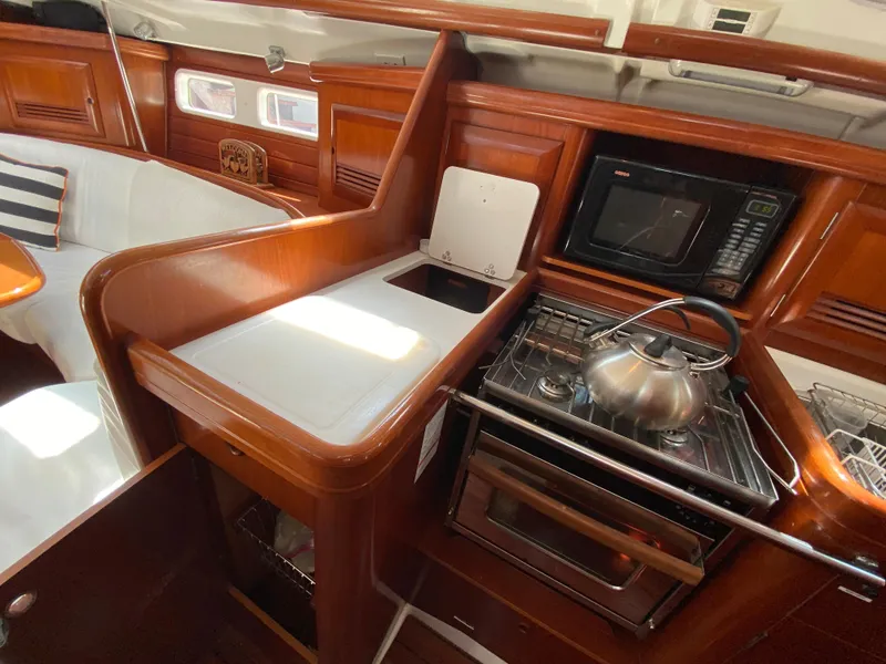Slide: The Image of 2003 Beneteau 423 yacht kitchen with stove, microwave, and wooden cabinetry. - 44