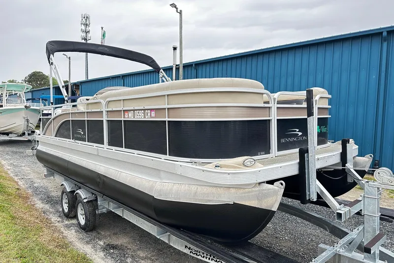 The Image of 2014 Bennington 2275SL Pontoon boat on trailer, parked near blue building. - 0