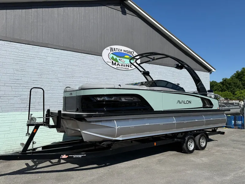 Slide: The Image of 2026 Avalon 2585 Excalibur pontoon boat on trailer outside marine shop. - 2
