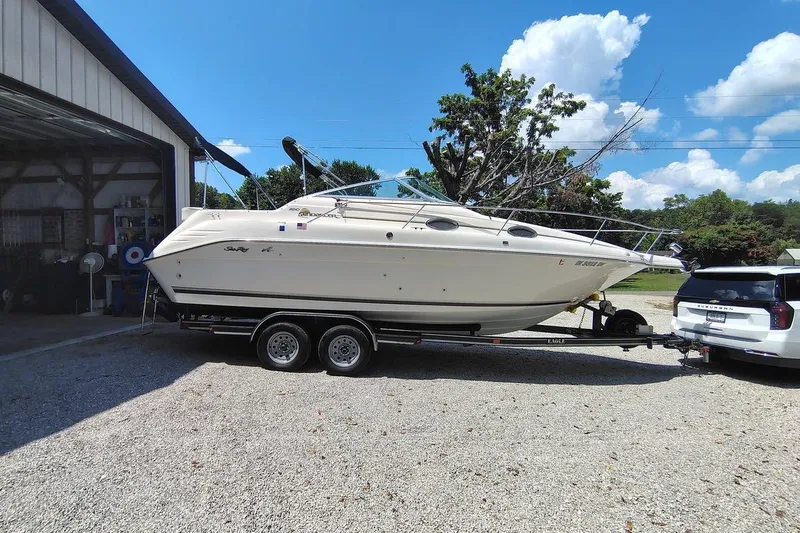 The Image of 1995 Sea Ray 250 Sundancer boat on trailer, parked beside a building under a clear sky. - 1