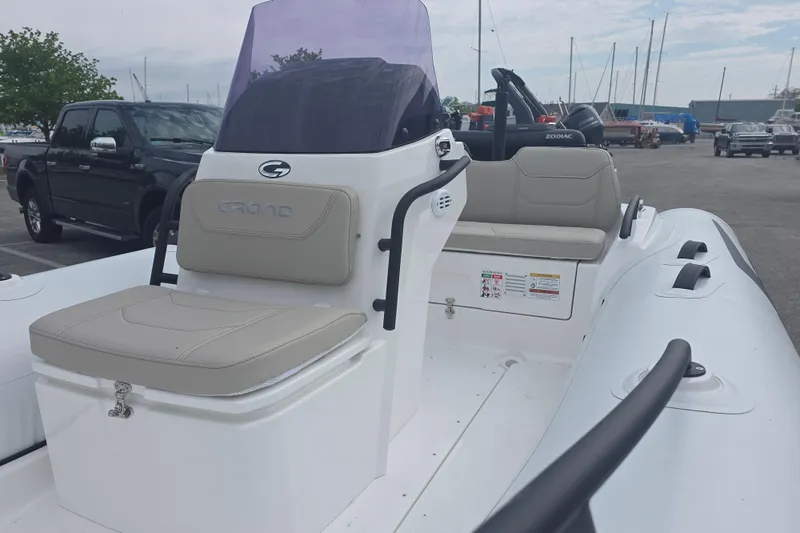 Slide: The Image of 2027 Grand Inflatables G420 boat with seating, parked near marina and vehicles. - 6