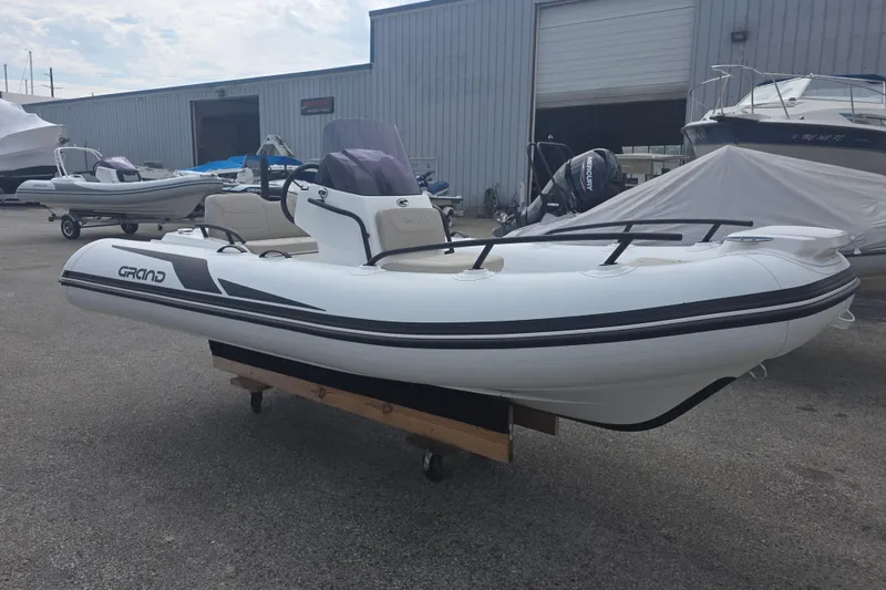 The Image of 2027 Grand Inflatables G420 boat displayed outdoors near a warehouse. - 0