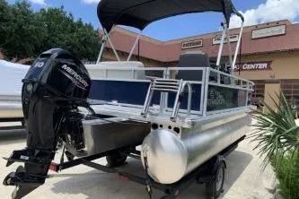 Slide: The Image of 2026 Sun Tracker Bass Buggy 16 XL Select pontoon boat with Mercury engine, parked outdoors. - 7