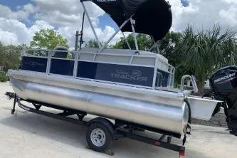 Slide: The Image of 2026 Sun Tracker Bass Buggy 16 XL Select pontoon boat on trailer, under a sunny sky. - 2