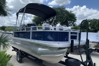 Slide: The Image of 2026 Sun Tracker Bass Buggy 16 XL Select pontoon boat on trailer, under a cloudy sky. - 5