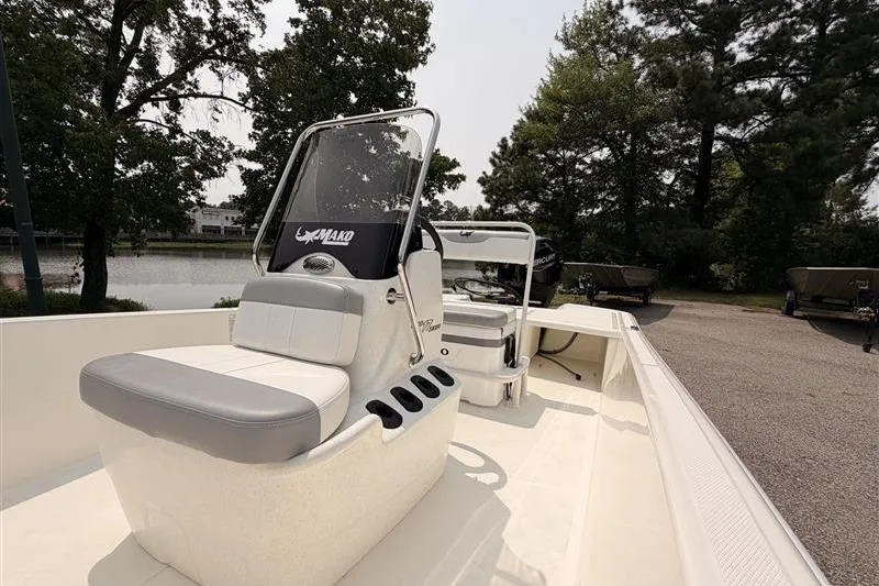 Slide: The Image of 2026 Mako Pro Skiff 17 CC boat interior with seating and console, parked near trees. - 9