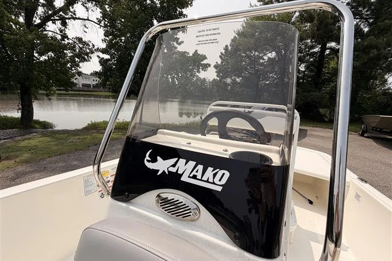 Slide: The Image of 2026 Mako Pro Skiff 17 CC boat console with steering wheel, near a serene lake. - 8