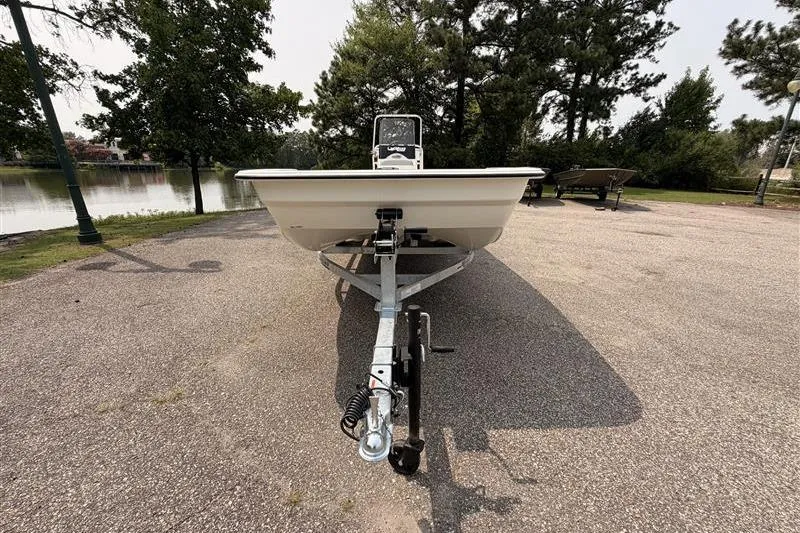 Slide: The Image of Front view of a 2026 Mako Pro Skiff 17 CC boat on a trailer by a lake. - 2
