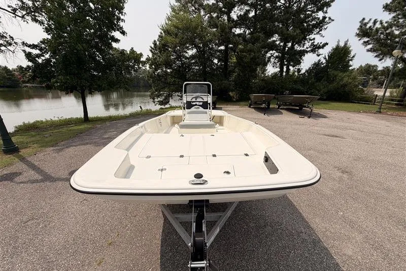 Slide: The Image of 2026 Mako Pro Skiff 17 CC boat on trailer near a lake and trees. - 1