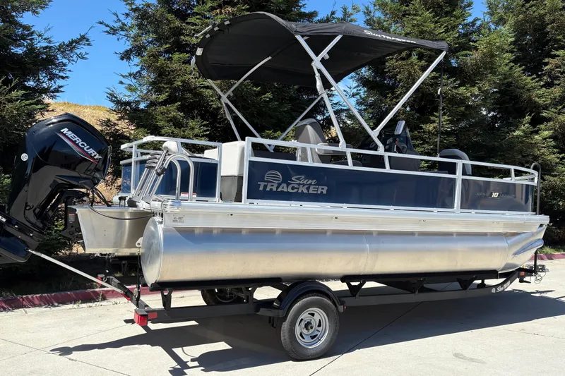 Slide: The Image of 2026 Sun Tracker Bass Buggy 18 DLX pontoon boat on trailer, parked outdoors. - 4