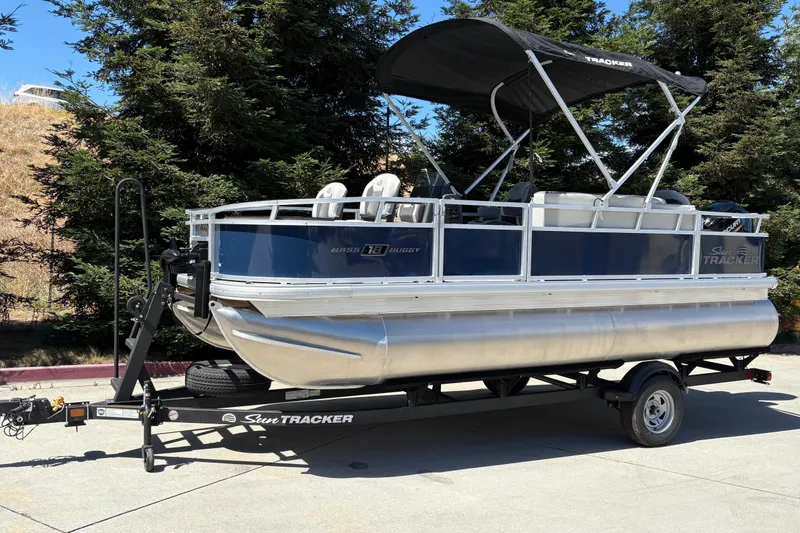 Slide: The Image of 2026 Sun Tracker Bass Buggy 18 DLX pontoon boat on trailer, parked outdoors. - 6