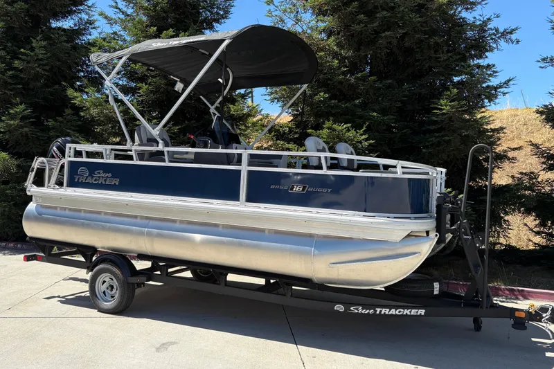 Slide: The Image of 2026 Sun Tracker Bass Buggy 18 DLX pontoon boat on trailer, parked outdoors. - 5