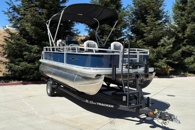 Slide: The Image of 2026 Sun Tracker Bass Buggy 18 DLX pontoon boat on trailer, parked outdoors. - 2